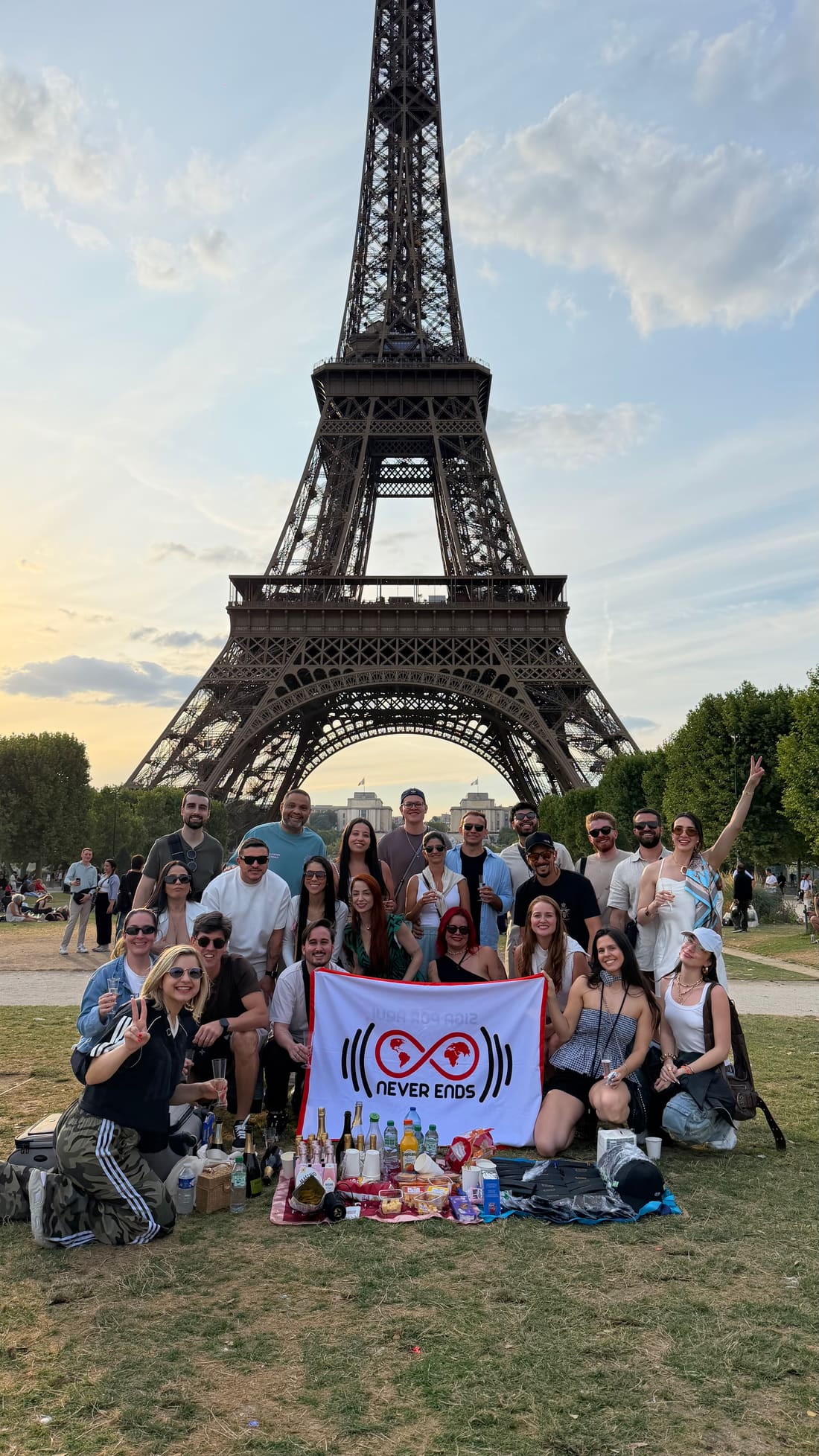 Grupo da Never Ends em piquenique aos pés da Torre Eiffel, em Paris, com a bandeira da agência