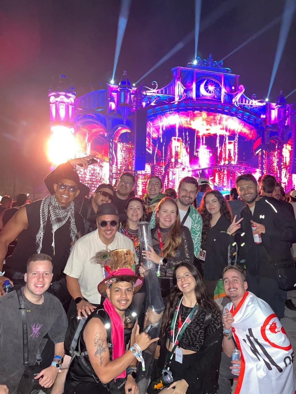 Grupo da Never Ends à noite diante de um palco da Tomorrowland Brasil iluminado de rosa e azul