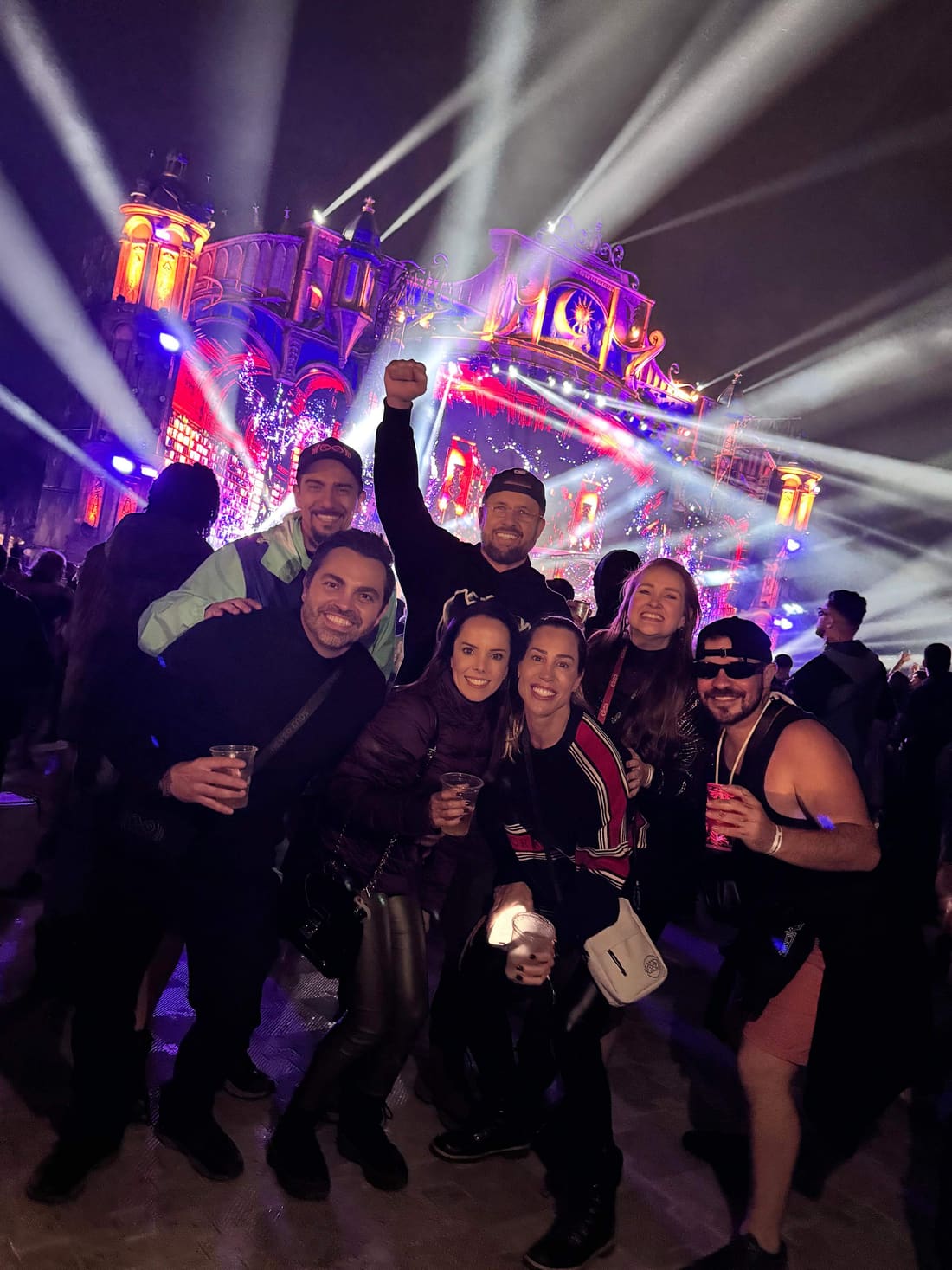 Grupo da Never Ends comemorando à noite no meio dos feixes de luz de um palco da Tomorrowland Brasil