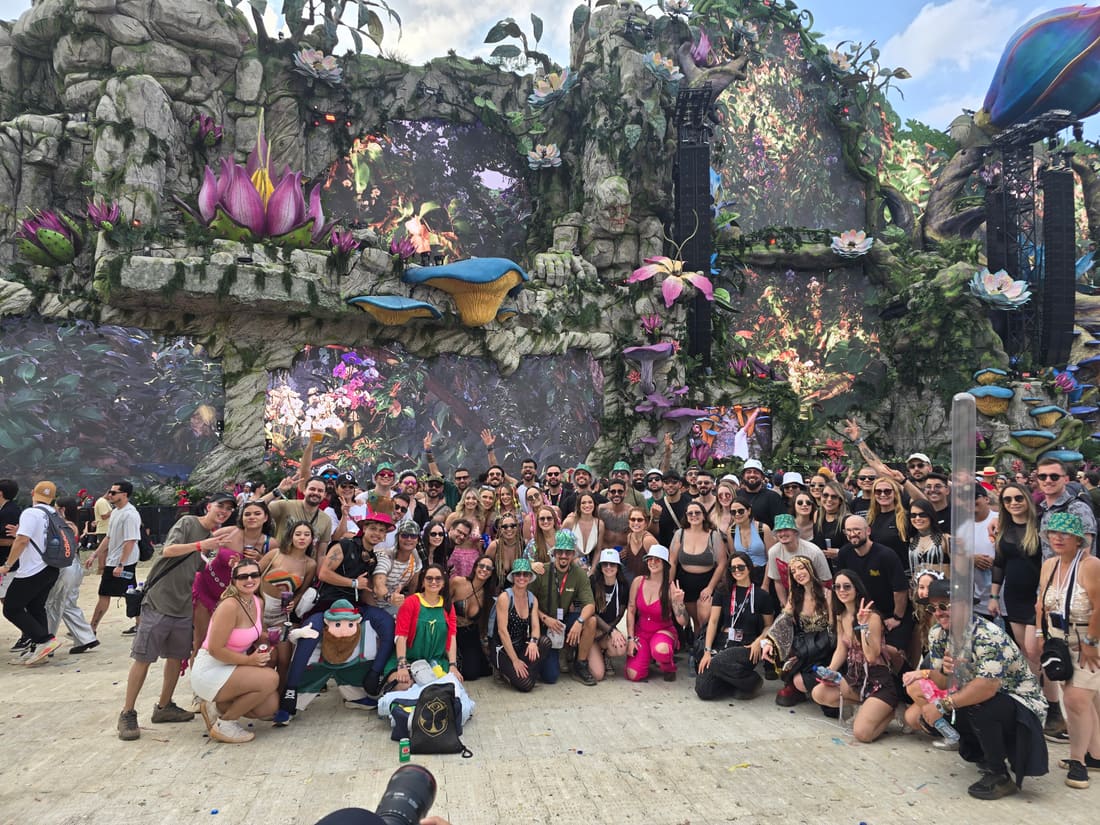 Grupo da Never Ends reunido de dia diante do Mainstage LIFE da Tomorrowland Brasil, cheio de flores gigantes, no Parque Maeda em Itu