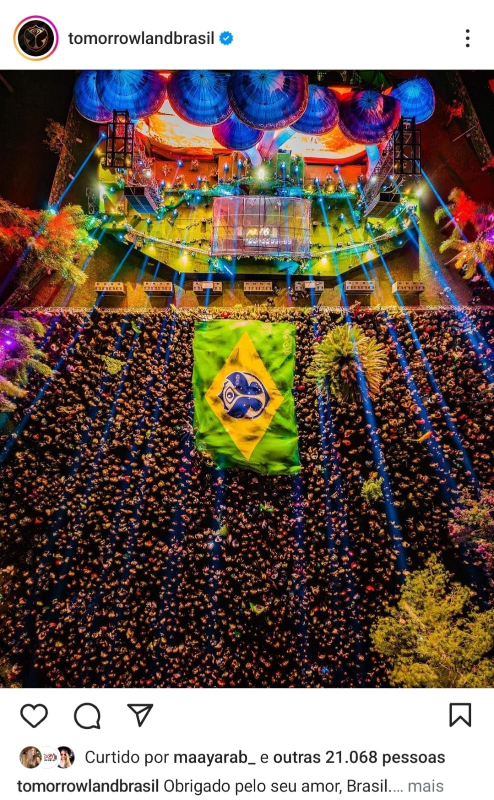 Publicação do perfil oficial da Tomorrowland Brasil mostrando a bandeira gigante do Brasil com o símbolo do festival aberta no meio do público, no Parque Maeda